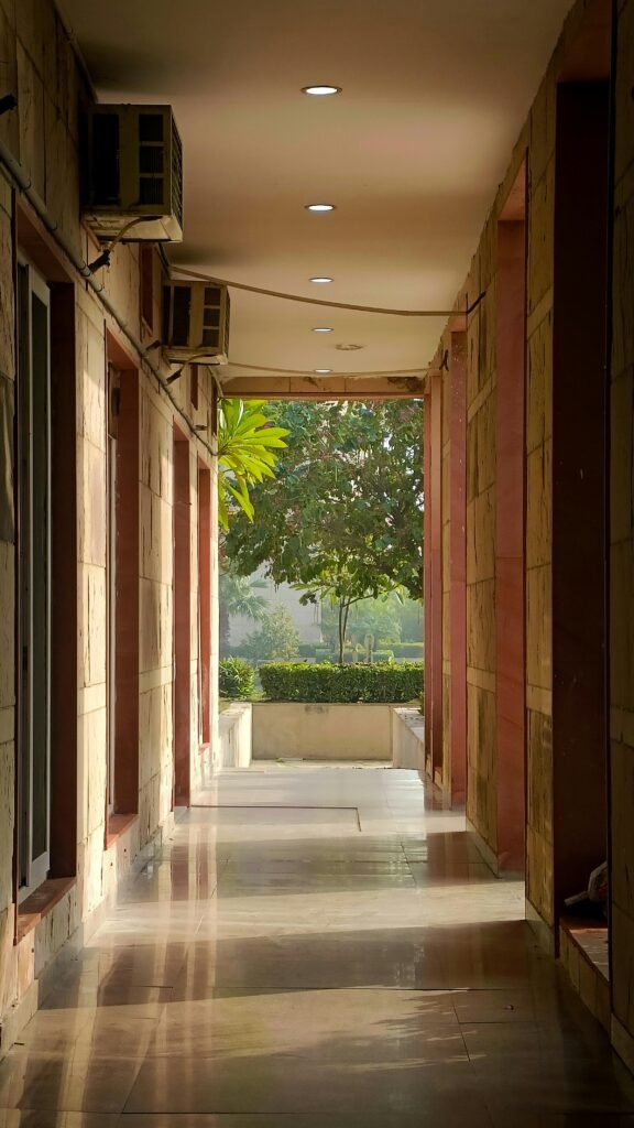 A sunlit corridor in Greater Noida, India with greenery visible outside, creating a serene ambiance.