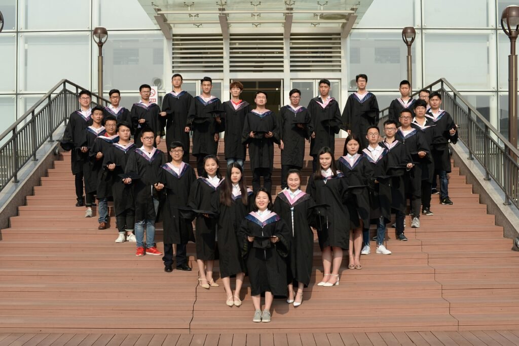 Large group of graduates in caps and gowns posing on campus stairs, celebrating academic achievement.